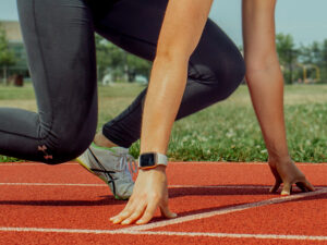 A cropped view of a runner on a track with hands holding steady and a foot ready to spring in action.