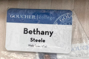 A blue and white employee badge wrapped in plastic reads "Goucher College" and the employee name "Bethany Steele"